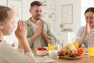 Photo of Family praying together before dinner at table indoors