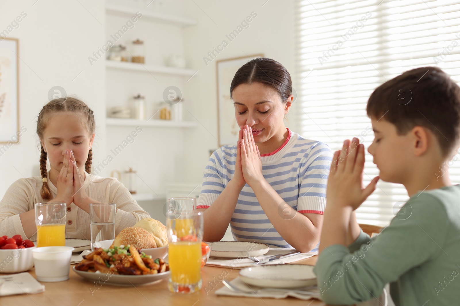 Family praying together before dinner at table indoors Photo of Family praying together before dinner at table indoors