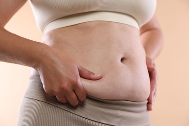 Photo of Woman with excessive belly fat on beige background, closeup. Overweight problem