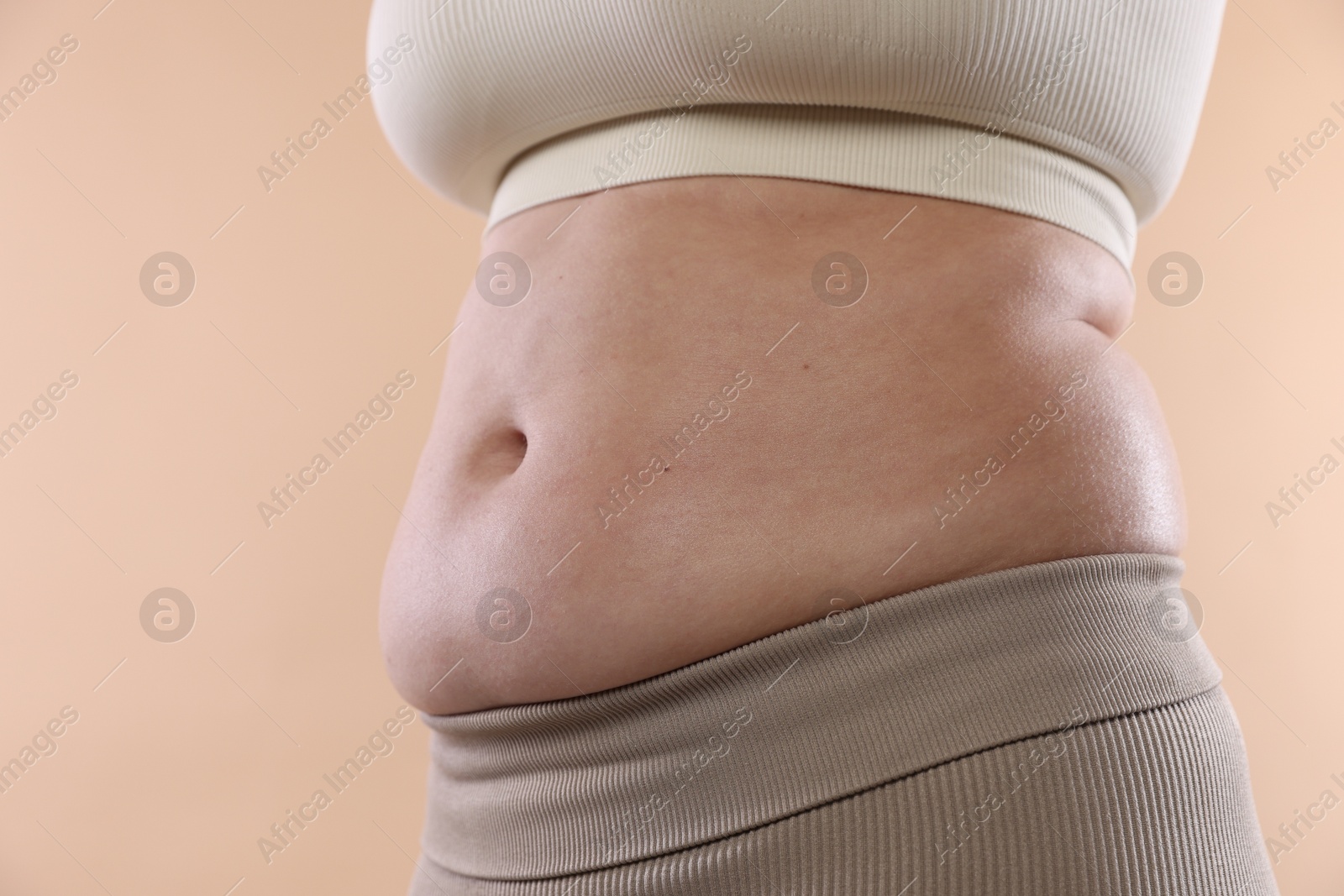 Woman with excessive belly fat on beige background, closeup. Overweight problem Photo of Woman with excessive belly fat on beige background, closeup. Overweight problem
