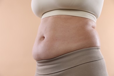 Photo of Woman with excessive belly fat on beige background, closeup. Overweight problem
