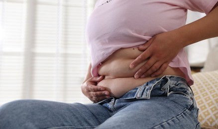 Photo of Woman with excessive belly fat at home, closeup and space for text. Overweight problem