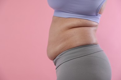 Photo of Woman with excessive belly fat on pink background, closeup and space for text. Overweight problem