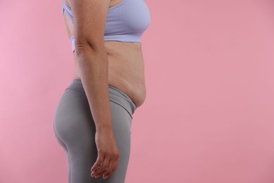 Photo of Woman with excessive belly fat on pink background, closeup and space for text. Overweight problem