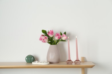 Photo of Elegant holders with burning candles, tulips in vase and other decor on wooden table near white wall