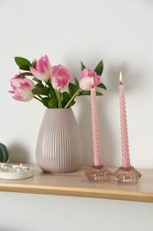 Photo of Elegant holders with burning candles, tulips in vase and other decor on wooden table near white wall