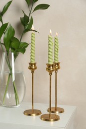 Photo of Elegant candlesticks with burning candles and branches in vase on dresser near beige wall