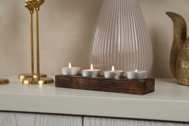 Photo of Elegant holders with burning candles and decor on dresser near beige wall, closeup