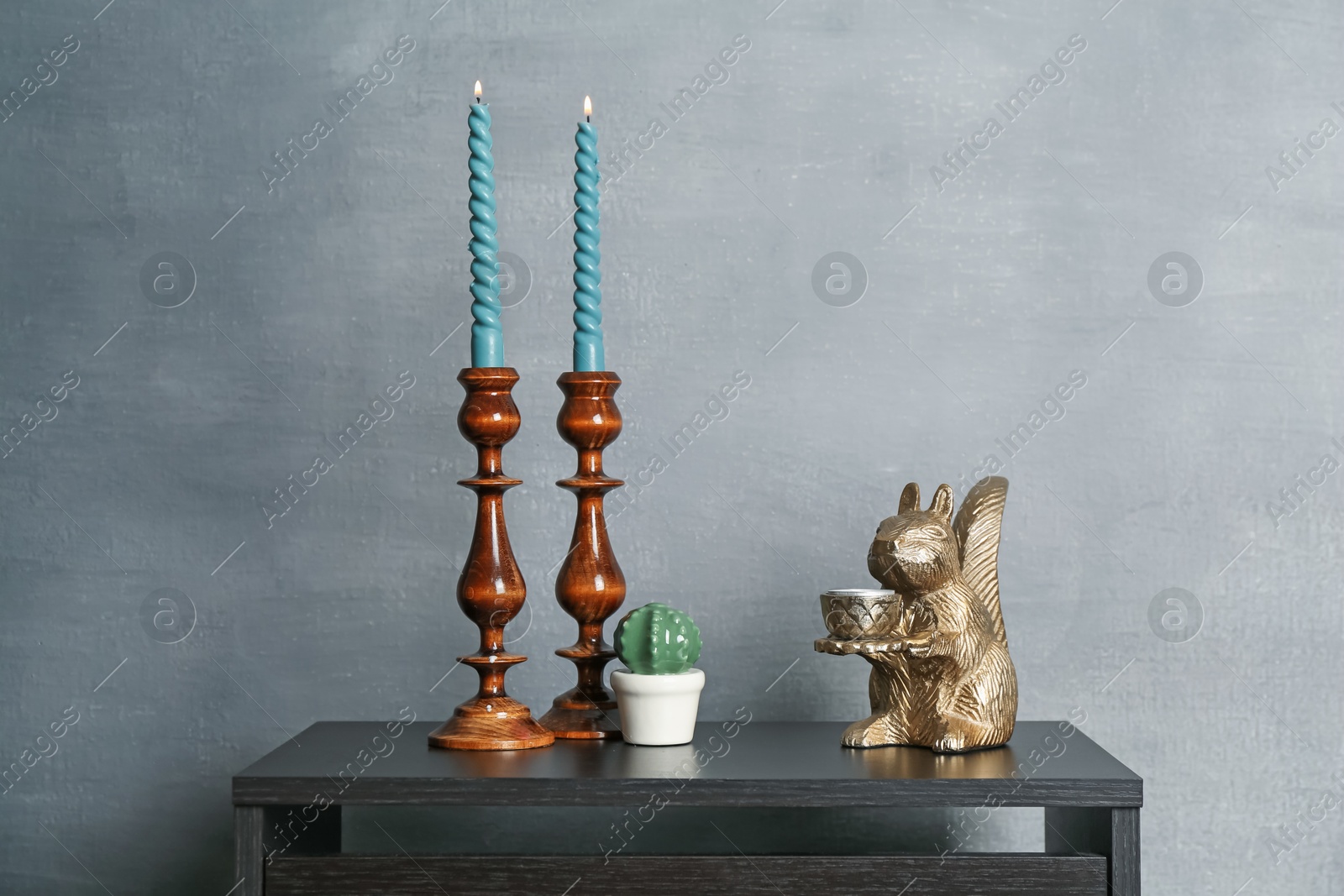 Elegant candlesticks with burning candles and other decor on black wooden table near grey wall Photo of Elegant candlesticks with burning candles and other decor on black wooden table near grey wall