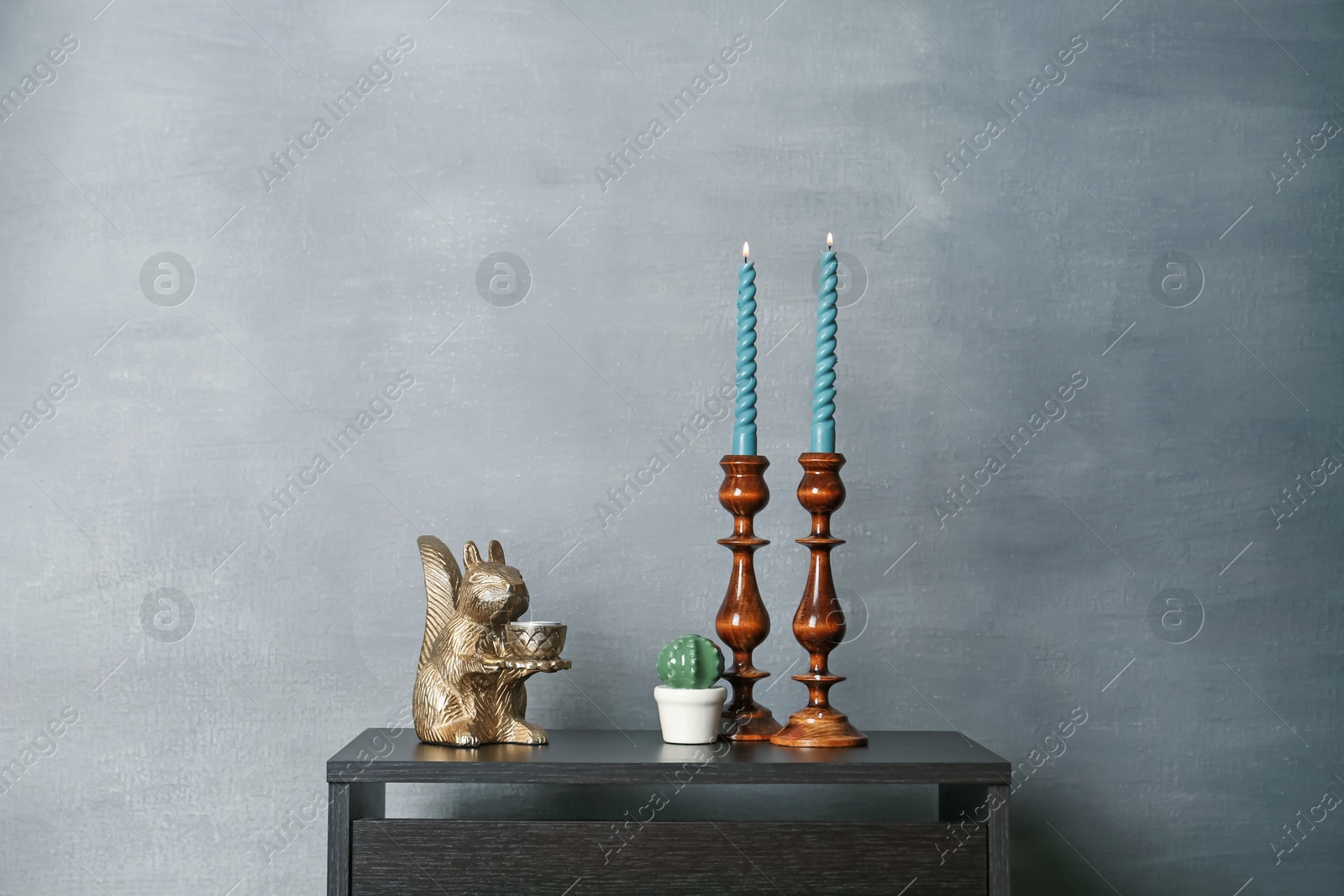Elegant candlesticks with burning candles and other decor on black wooden table near grey wall Photo of Elegant candlesticks with burning candles and other decor on black wooden table near grey wall