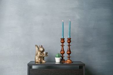 Photo of Elegant candlesticks with burning candles and other decor on black wooden table near grey wall