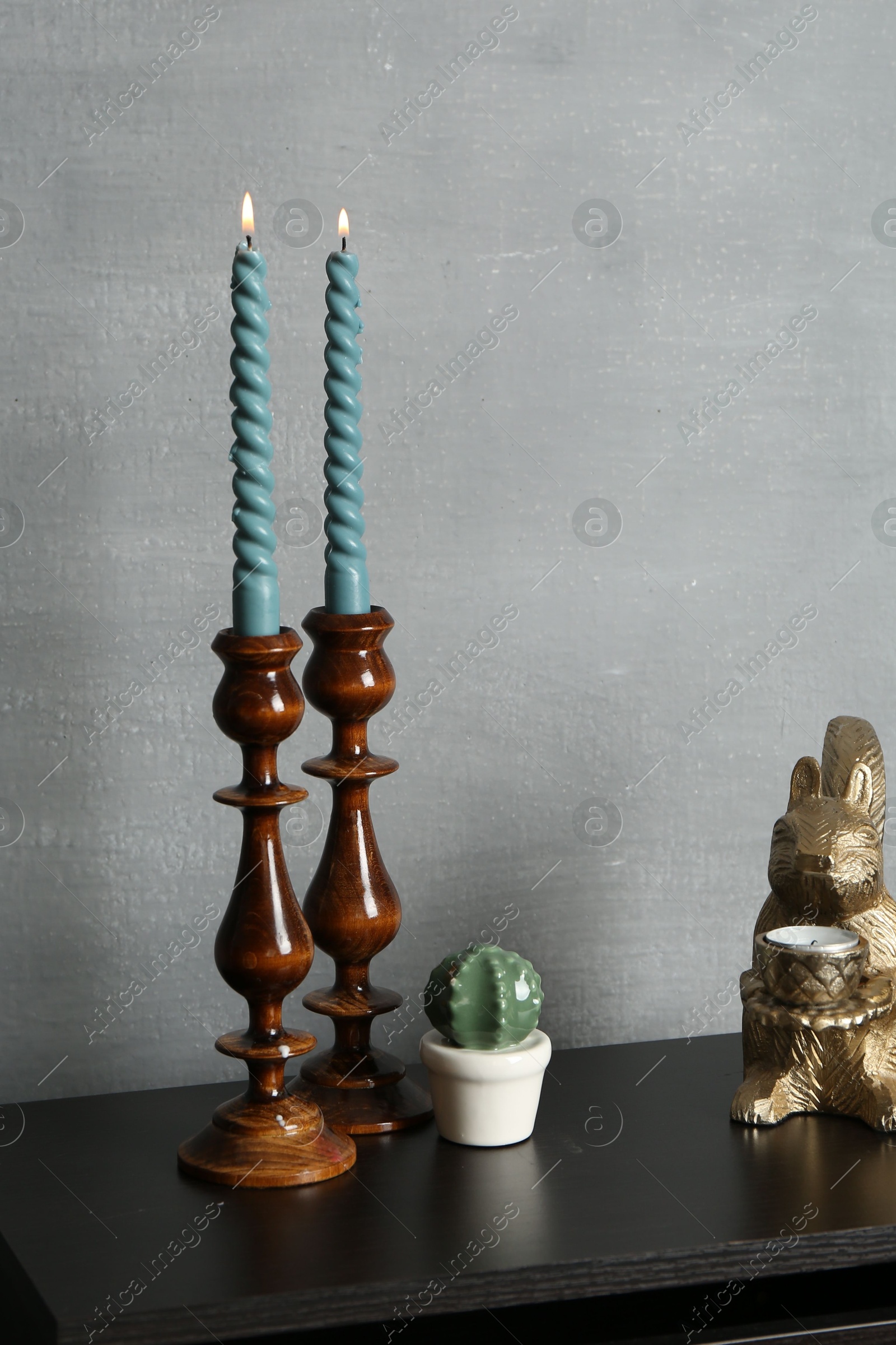 Elegant candlesticks with burning candles and other decor on black wooden table near grey wall Photo of Elegant candlesticks with burning candles and other decor on black wooden table near grey wall