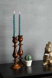 Photo of Elegant candlesticks with burning candles and other decor on black wooden table near grey wall