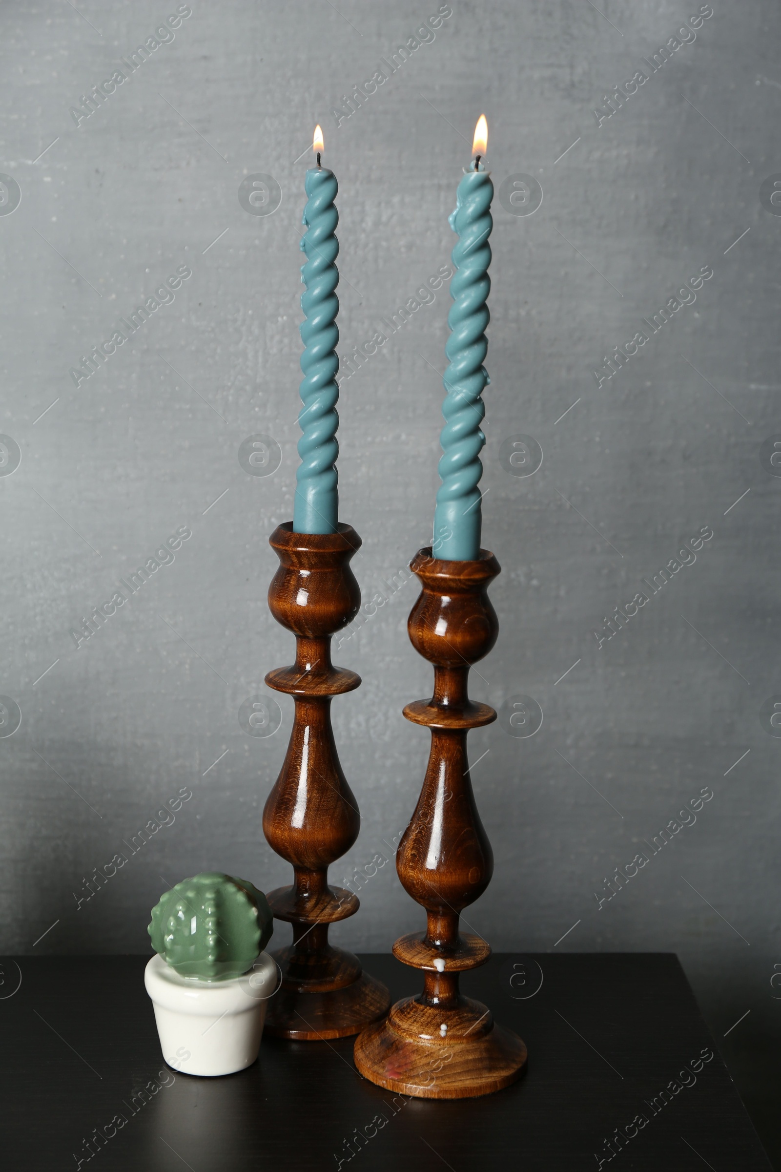 Elegant candlesticks with burning candles and other decor on black wooden table near grey wall Photo of Elegant candlesticks with burning candles and other decor on black wooden table near grey wall