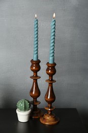 Photo of Elegant candlesticks with burning candles and other decor on black wooden table near grey wall