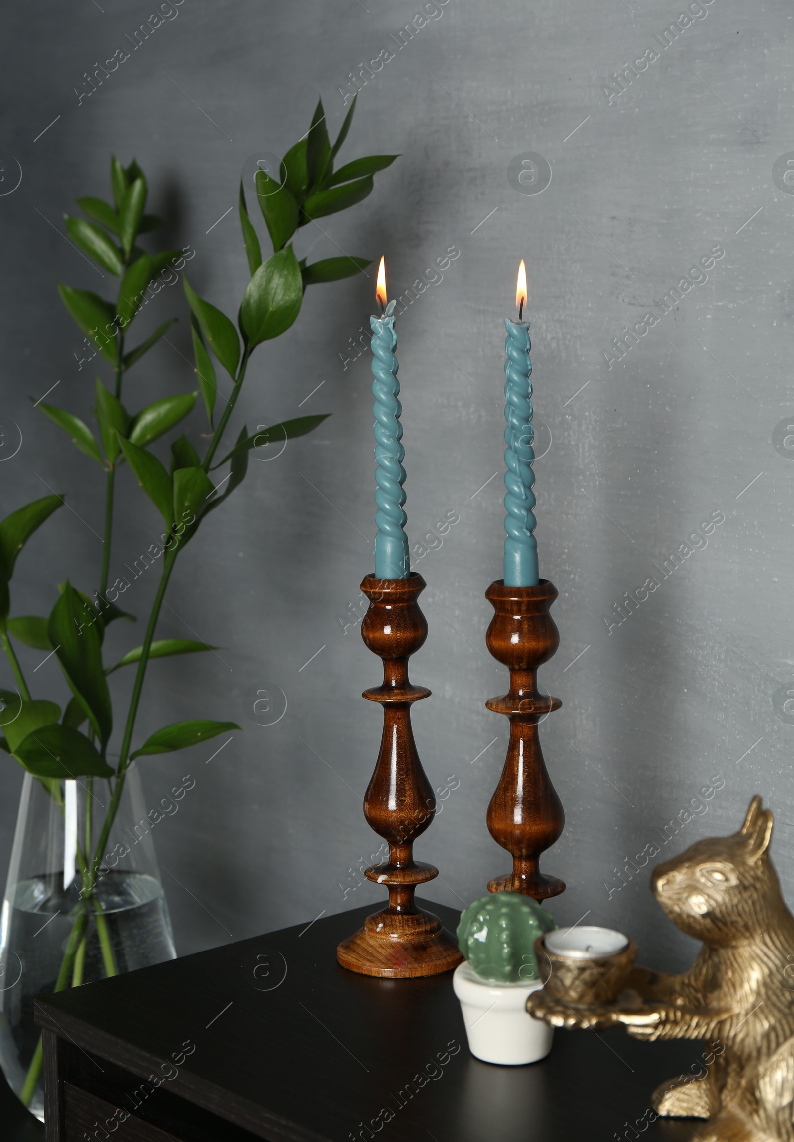 Elegant candlesticks with burning candles, branches in vase and other decor on dresser near grey wall Photo of Elegant candlesticks with burning candles, branches in vase and other decor on dresser near grey wall