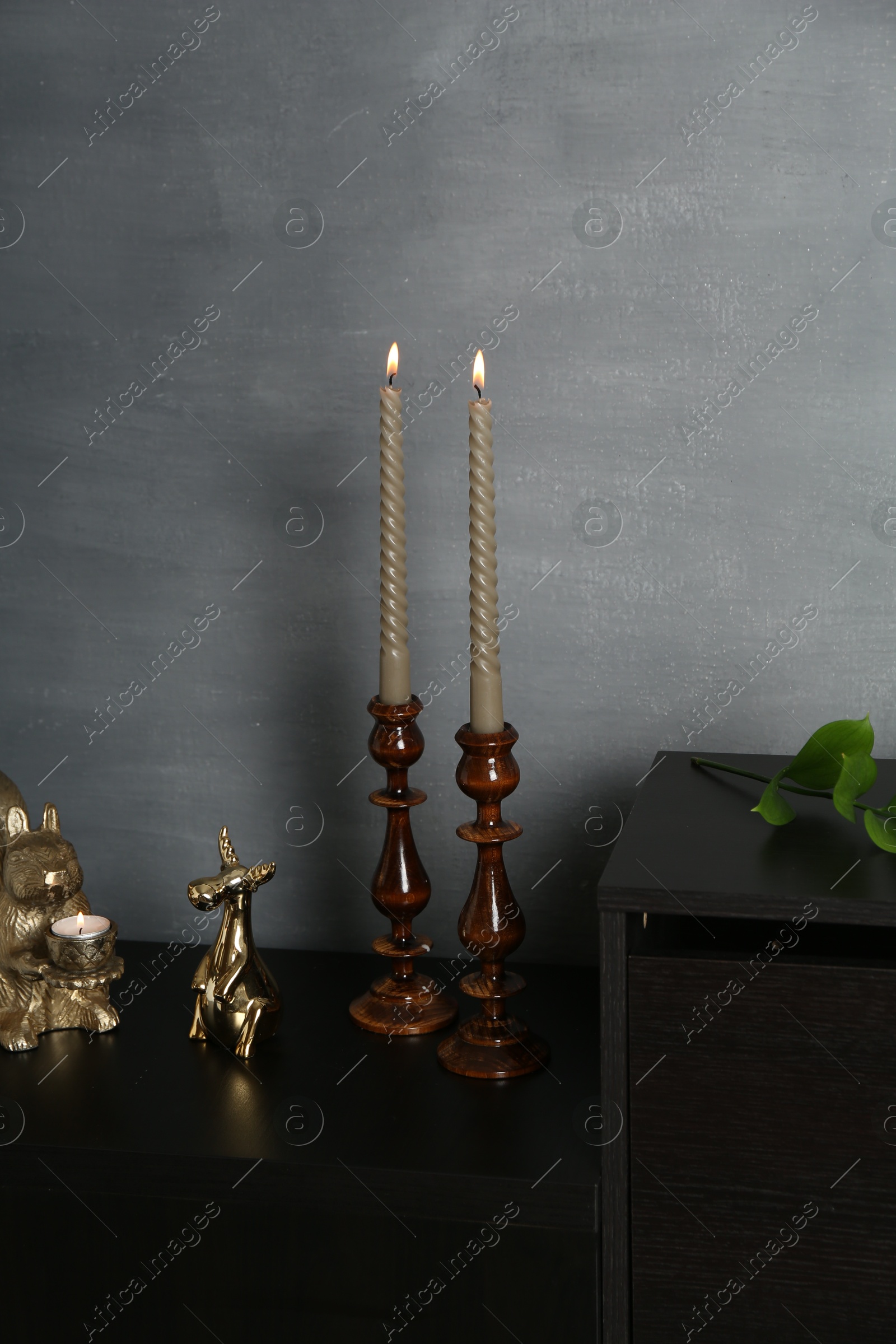 Elegant candlesticks with burning candles and other decor on dresser near grey wall Photo of Elegant candlesticks with burning candles and other decor on dresser near grey wall
