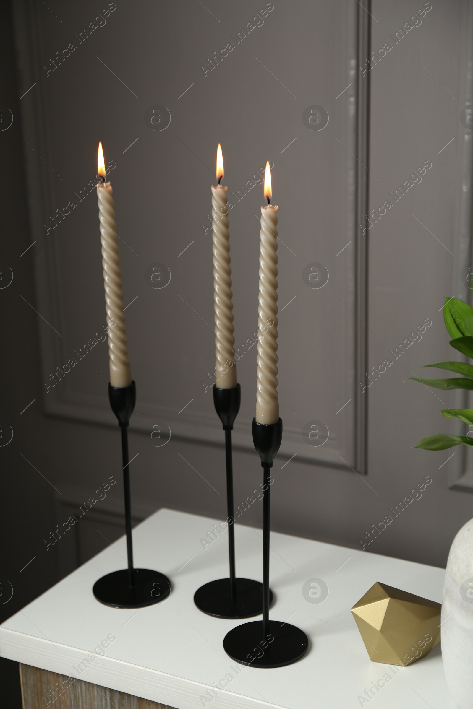Photo of Elegant candlesticks with burning candles and other decor on dresser near grey wall