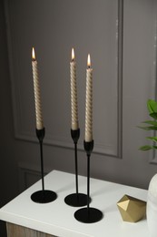 Photo of Elegant candlesticks with burning candles and other decor on dresser near grey wall