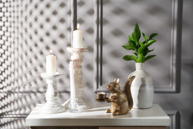 Photo of Elegant candlesticks with burning candles, branches in vase and other decor on dresser near grey wall