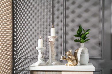 Photo of Elegant candlesticks with burning candles, branches in vase and other decor on dresser near grey wall