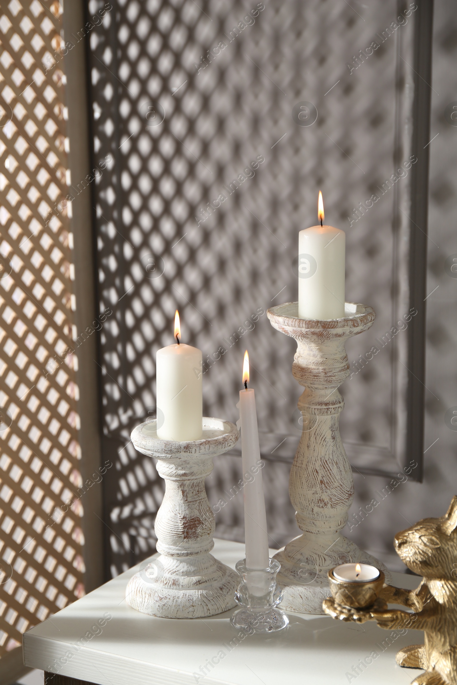 Elegant candlesticks with burning candles and other decor on dresser near grey wall Photo of Elegant candlesticks with burning candles and other decor on dresser near grey wall