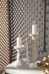 Photo of Elegant candlesticks with burning candles and other decor on dresser near grey wall
