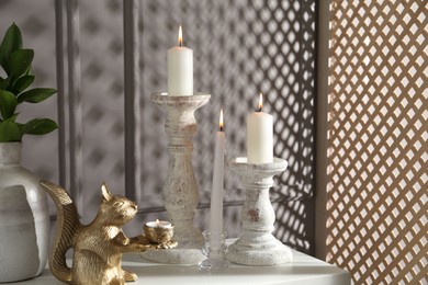 Photo of Elegant candlesticks with burning candles, branches in vase and other decor on dresser near grey wall
