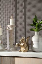 Photo of Elegant candlesticks with burning candles, branches in vase and other decor on dresser near grey wall