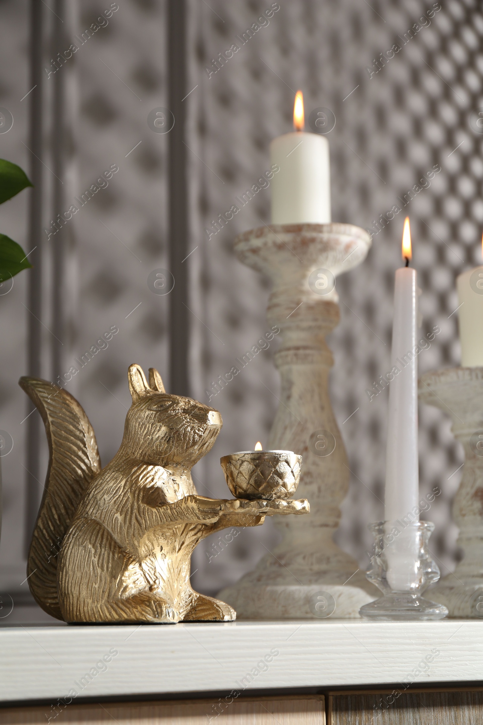 Elegant candlesticks with burning candles and other decor on dresser near grey wall Photo of Elegant candlesticks with burning candles and other decor on dresser near grey wall