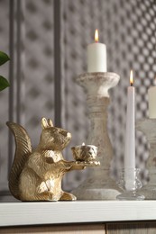Photo of Elegant candlesticks with burning candles and other decor on dresser near grey wall