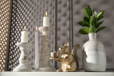 Photo of Elegant candlesticks with burning candles, branches in vase and other decor on dresser near grey wall