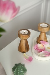 Photo of Elegant candlesticks with burning candles and flower petals on dresser near white wall