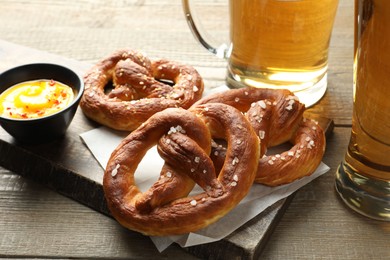 Photo of Tasty pretzels, sauce and beer on wooden table, closeup