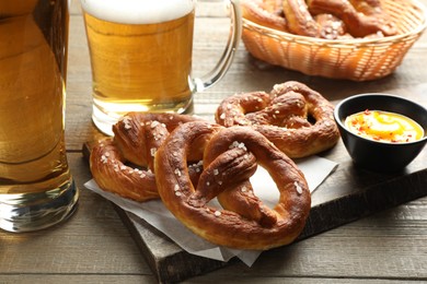 Photo of Tasty pretzels, sauce and beer on wooden table, closeup
