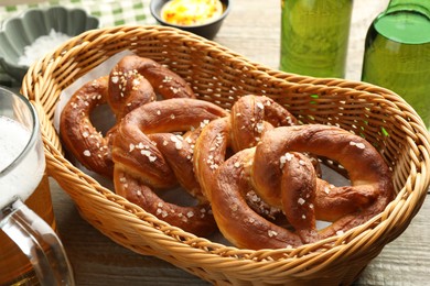Photo of Tasty pretzels in basket and beer on wooden table, closeup