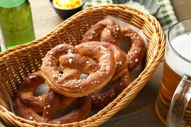 Photo of Tasty pretzels in basket and beer on wooden table, closeup