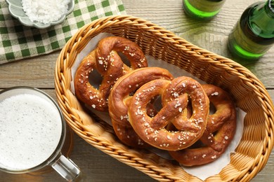 Photo of Tasty pretzels in basket and beer on wooden table, flat lay