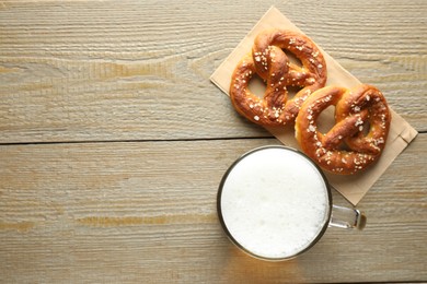 Photo of Tasty pretzels and glass mug of beer on wooden table, flat lay. Space for text