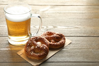 Photo of Tasty pretzels and glass mug of beer on wooden table, closeup. Space for text