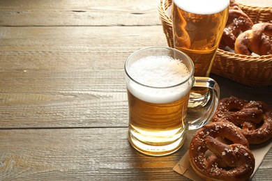 Photo of Tasty pretzels and glass mugs of beer on wooden table, closeup. Space for text