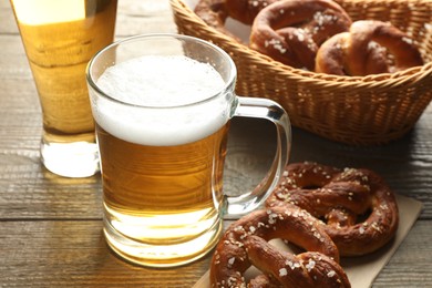 Photo of Tasty pretzels and glass mugs of beer on wooden table, closeup