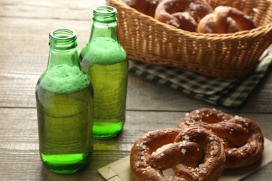 Photo of Tasty pretzels and bottles of beer on wooden table, closeup