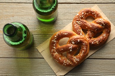 Photo of Tasty pretzels and bottles of beer on wooden table, flat lay