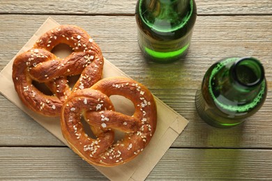 Photo of Tasty pretzels and bottles of beer on wooden table, flat lay