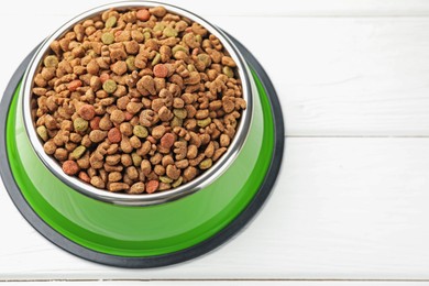 Photo of Dry pet food in feeding bowl on white wooden background, closeup