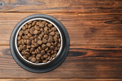 Photo of Dry pet food in feeding bowl on wooden background, top view. Space for text