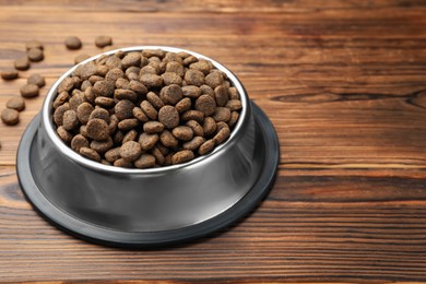 Photo of Dry pet food in feeding bowl on wooden background, closeup