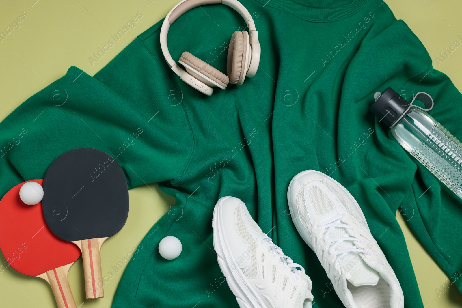 Sportswear, sneakers, water bottle, headphones, ping pong rackets and balls on pale olive background, flat lay Photo of Sportswear, sneakers, water bottle, headphones, ping pong rackets and balls on pale olive background, flat lay