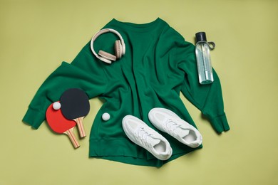 Photo of Sportswear, sneakers, water bottle, headphones, ping pong rackets and balls on pale olive background, flat lay